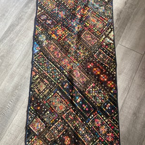 以下が含まれることがあります： カラフルな布の切れ端でダイヤモンドパターンが作られた、黒いタペストリー。スパンコールとビーズで飾られています。