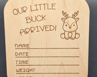 Puede incluir: Placa de madera clara con esquinas redondeadas. El texto "OUR LITTLE BUCK ARRIVED!" está grabado en la parte superior, con una ilustración de ciervo de dibujos animados a la derecha. Debajo hay líneas etiquetadas como "NAME", "DATE", "TIME", "WEIGHT" y "LENGTH".