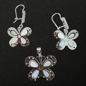 May include: A set of silver butterfly earrings and a pendant necklace. The earrings have a delicate butterfly design with cutouts and a white enamel finish. The pendant is similar in design and features a loop for attaching to a chain.