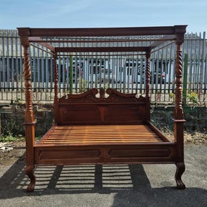 Puede incluir: Una cama con dosel grande hecha de madera de color marrón oscuro. La cama cuenta con cuatro postes esquineros altos y retorcidos, un cabecero con detalles tallados intrincados en la parte superior y una base de listones, apoyada sobre cuatro patas curvas.