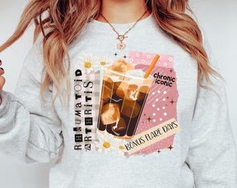 May include: A light gray sweatshirt with a graphic of an iced coffee drink with the words "Rheumatoid Arthritis" and "Bonus Flare Days". The design includes daisies and a pink background with the words "chronic iconic".