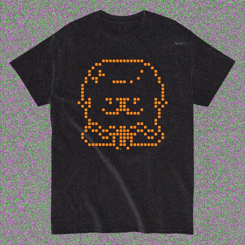 May include: Black t-shirt featuring an orange pixelated graphic of a cartoon animal face. The design is centered on the front of the shirt. The shirt has short sleeves and a crew neck.