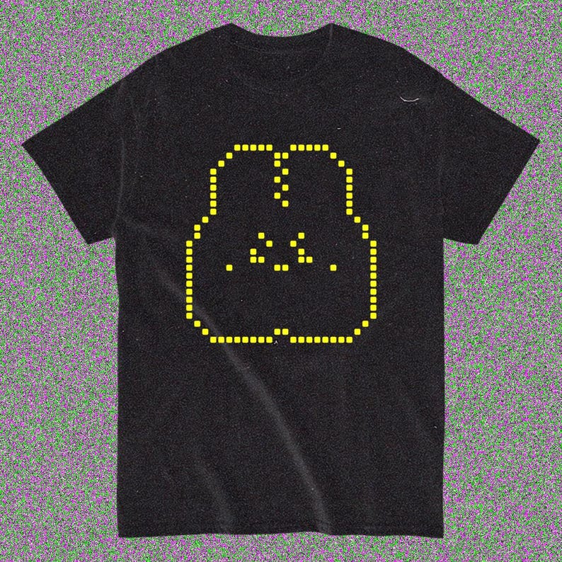 May include: Black t-shirt with a yellow pixelated face design. The face is outlined with small yellow squares, with yellow dots for the eyes and mouth. The shirt is made of a soft material.