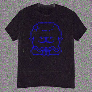 May include: Black t-shirt featuring a pixelated blue graphic of a dog's face. The design is made up of small blue squares, creating a retro, digital aesthetic. The shirt has a classic crew neck and short sleeves.