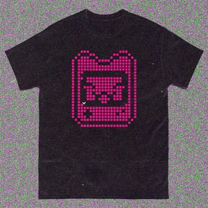May include: Black t-shirt with a pixelated pink graphic of a retro handheld gaming device. The design is centered on the shirt and is made up of small, square pixels. The t-shirt has a classic crew neck.