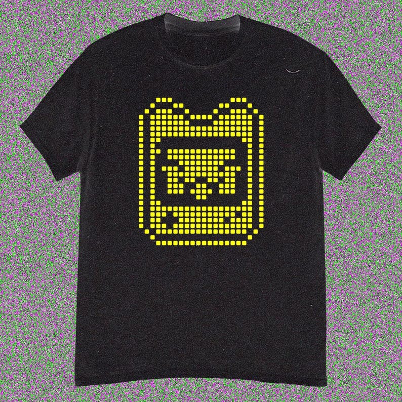 May include: Black t-shirt with a yellow pixelated graphic of a handheld gaming device. The design is in the centre of the shirt. The t-shirt has short sleeves and a crew neck.