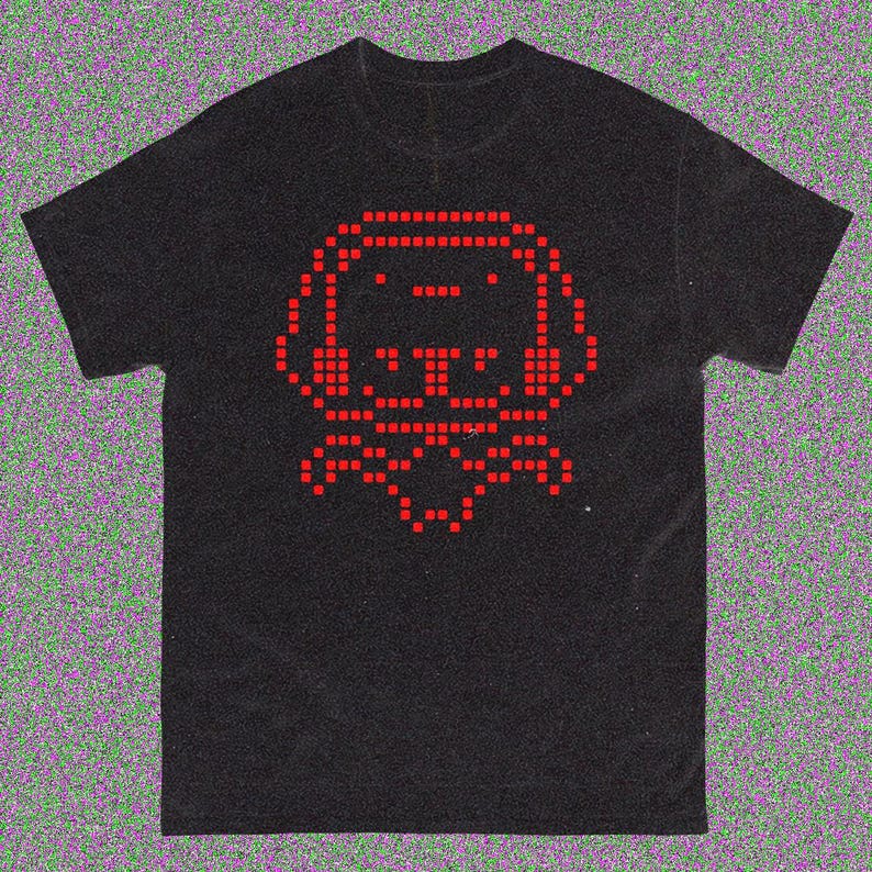 May include: Black t-shirt with a red pixelated dog graphic. The dog wears headphones and a bow tie. The design is created from small squares, giving a retro video game feel. The shirt is made of a soft material.