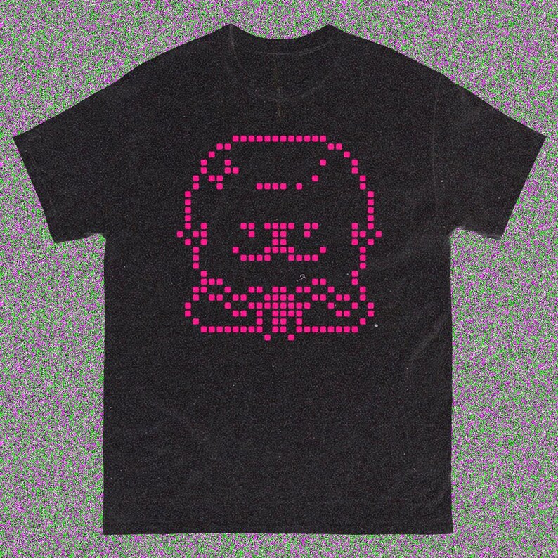 May include: Black t-shirt featuring a pixelated pink graphic of a cartoon animal. The design is centered on the front of the shirt. The t-shirt has a crew neck and short sleeves.