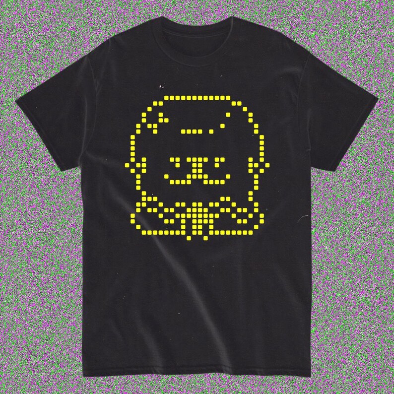 May include: Black t-shirt featuring a pixelated yellow cat design. The cat's face and body are formed by small squares, giving it a retro video game aesthetic. The shirt is made of a soft material.