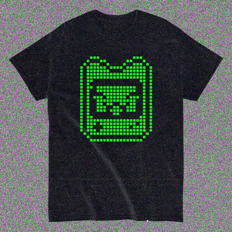 May include: Black t-shirt with a green pixelated graphic of a handheld gaming device. The design is in the centre of the shirt. The t-shirt has short sleeves and a crew neck.