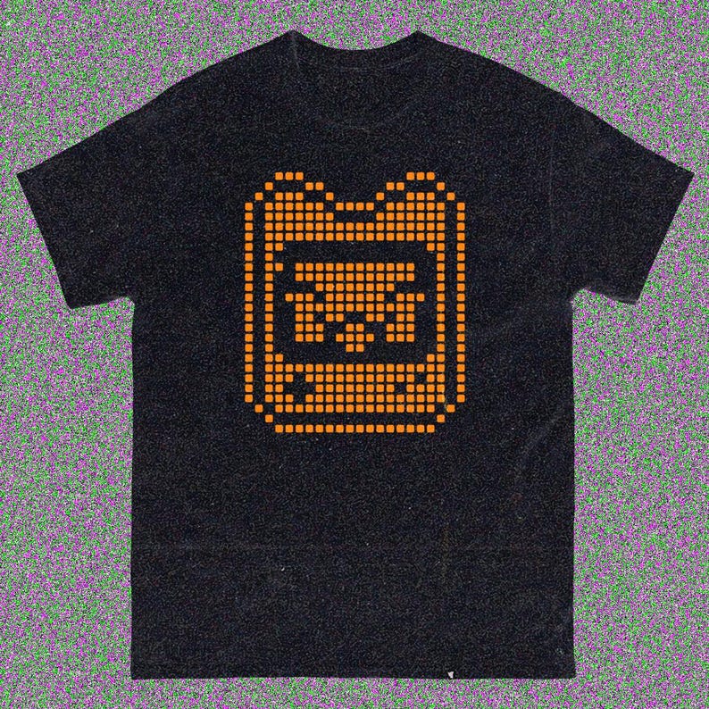 May include: Black t-shirt with an orange pixelated graphic. The graphic is a stylized design of a rectangular shape with a central image. The shirt has short sleeves and a crew neck.