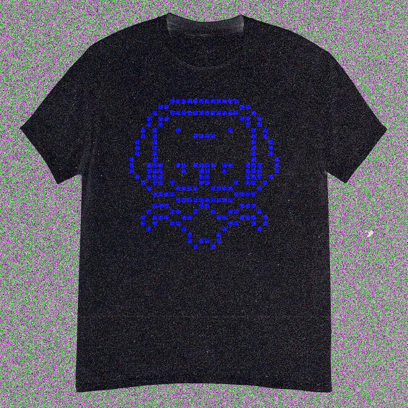 May include: Black t-shirt with a blue pixelated dog design. The dog's image is formed from small blue squares, creating a retro digital look. The shirt has a crew neck and short sleeves.