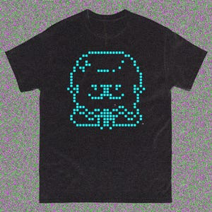 May include: Black t-shirt featuring a pixelated teal graphic of a smiling creature. The design is centered on the shirt and is made up of small squares. The shirt has short sleeves and a crew neck.