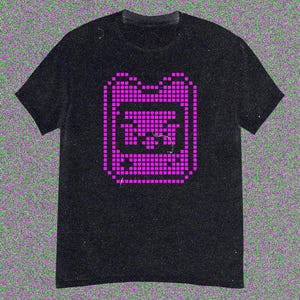 May include: Black t-shirt with a magenta pixelated graphic of a retro handheld gaming device. The design, made of small squares, is centrally placed. The shirt has short sleeves and a crew neck.
