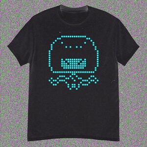 May include: Black t-shirt featuring a pixelated blue graphic of a smiling, blob-like creature. The design is made up of small squares, giving it a retro video game aesthetic. The shirt has a crew neck and short sleeves.