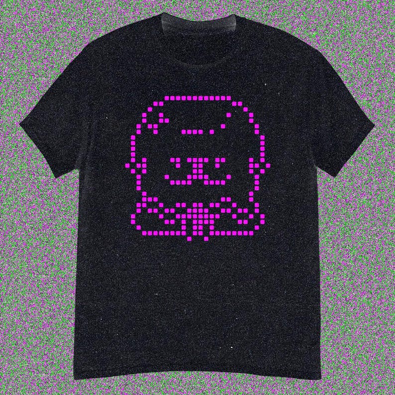 May include: Black t-shirt featuring a pixelated pink cat design. The cat's face and body are formed by small, square pixels, creating a retro aesthetic. The shirt has short sleeves and a crew neck.