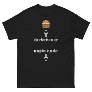 Puede incluir: Camiseta negra con un gráfico de hamburguesa pixelada. Encima de la hamburguesa, el texto dice "Quarter Pounder" con una flecha hacia arriba. Debajo, el texto dice "Daughter Pounder" con una flecha hacia abajo. Diseño humorístico.