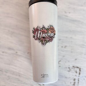 May include: White stainless steel tumbler with a floral design and the word "Mama" in pink lettering. The tumbler has a black lid and the word "slim" printed on the bottom.