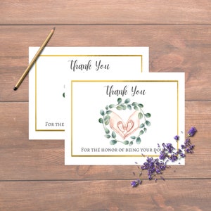 May include: Two white thank you cards with gold borders and elegant script. One card features a watercolor illustration of hands cradling baby feet within a green wreath. The text reads "Thank You" and "For the honor of being your doula."