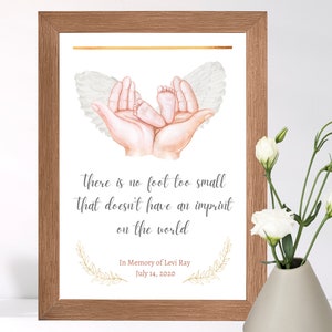 May include: A framed print featuring a watercolour illustration of two hands holding a pair of tiny baby feet with angel wings. The text reads "There is no foot too small that doesn't have an imprint on the world." Below the illustration is the text "In Memory of Levi Ray July 14, 2020".