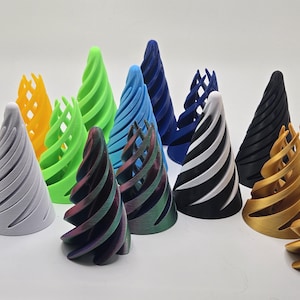 Könnte beinhalten: Eine Sammlung von 11 3D-gedruckten kegelförmigen Objekten in verschiedenen Farben, darunter Gelb, Weiß, Grün, Blau, Schwarz und Gold. Jeder Kegel hat ein einzigartiges Muster oder eine einzigartige Textur.