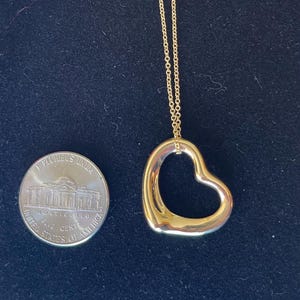 May include: A gold chain necklace with a large open heart pendant. The pendant is about the size of a US nickel.