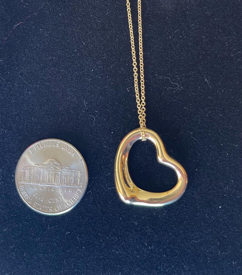 May include: A gold chain necklace with a large open heart pendant. The pendant is about the size of a US nickel.