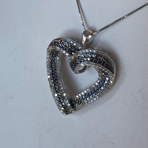 May include: A silver necklace with a heart-shaped pendant. The pendant is made of two intertwined hearts, one with white diamonds and the other with black diamonds.