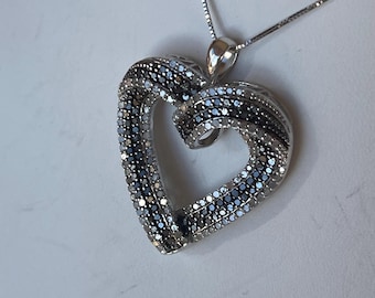 Puede incluir: Un collar de plata con un colgante en forma de corazón. El colgante está hecho de dos corazones entrelazados, uno con diamantes blancos y el otro con diamantes negros.