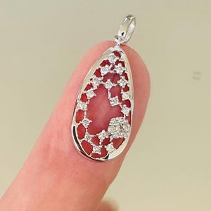 May include: A teardrop-shaped pendant with a silver frame, featuring a red coral center and sparkling white gemstones. The pendant is designed with an openwork pattern, creating a delicate and elegant look. The bail is also silver.