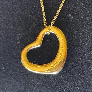 May include: A gold chain necklace with a large open heart pendant. The pendant is engraved with "Tiffany & Co. 925."