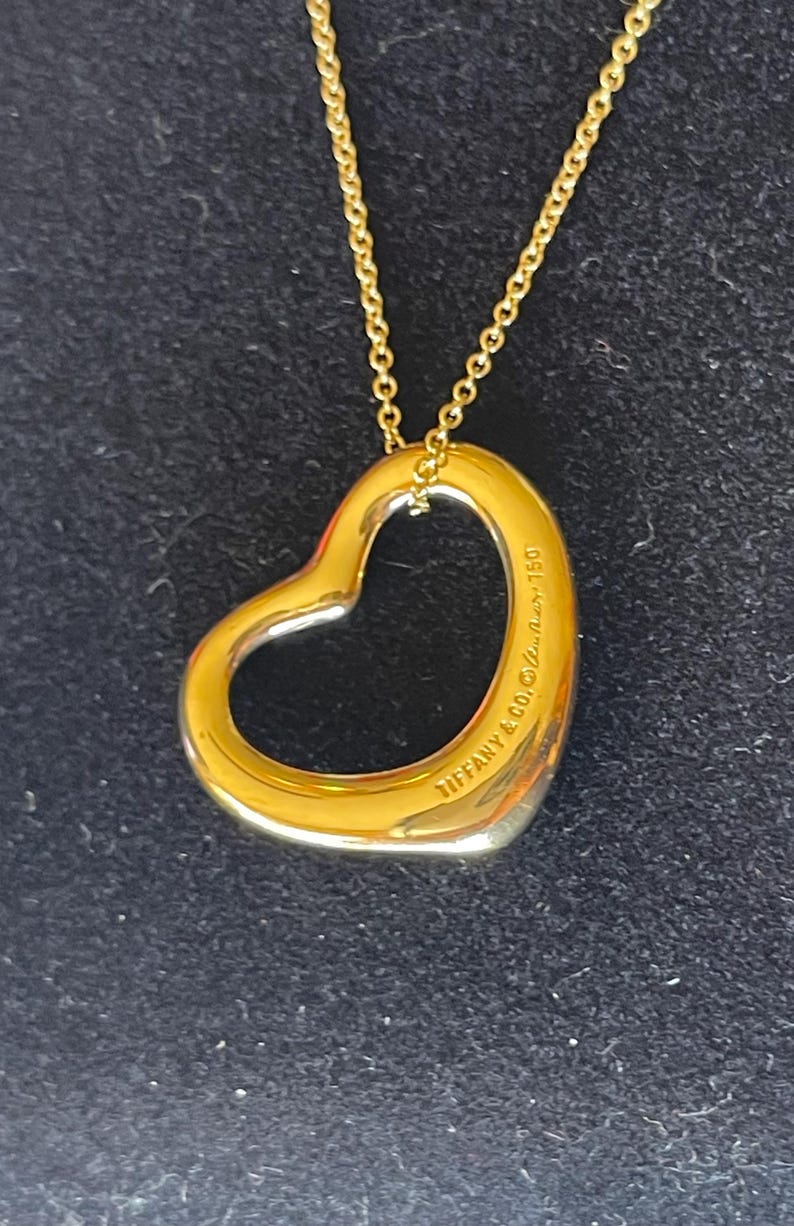 May include: A gold chain necklace with a large open heart pendant. The pendant is engraved with "Tiffany & Co. 925."