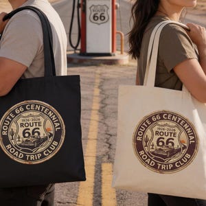 May include: Two tote bags, one black and one off-white, each featuring a circular Route 66 Centennial design. The design includes the text "Route 66", "1926-2026", and "Road Trip Club", with a vintage car illustration.