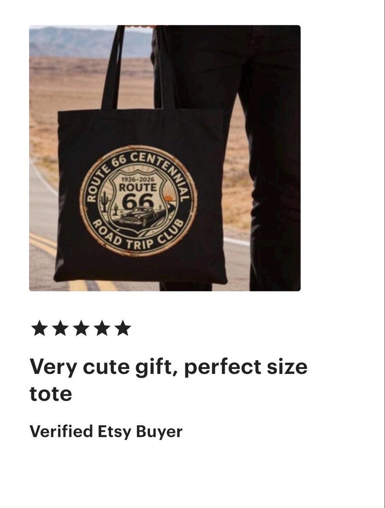 May include: Black tote bag featuring a Route 66 Centennial design with a classic car illustration. The design includes the text "Route 66 Road Trip Club" and the years 1926-2026. The bag is held by a person.
