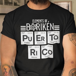 Puede incluir: Camiseta negra con un diseño gráfico blanco que presenta el texto "ELEMENTS OF, =BORIKEN=". El gráfico incluye un símbolo de elemento químico estilizado para cada letra de la palabra "PUERTO RICO" con el nombre del elemento correspondiente y el peso atómico debajo de cada símbolo.