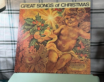 May include: Vintage vinyl record album cover titled "Great Songs of Christmas." The cover features a cherub with wings, surrounded by Christmas foliage and a radiant starburst. The color palette includes warm tones of orange, brown, and gold.