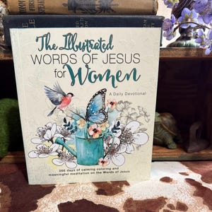 May include: A book titled "The Illustrated Words of Jesus for Women" with a floral and butterfly design. The cover features a bird, a blue butterfly, and a teal watering can. The book is a daily devotional with 366 days of calming coloring and meditation.