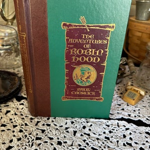 May include: A green and brown hardcover book titled "The Adventures of Robin Hood" by Paul Creswick. The cover features a scroll with an illustration of Robin Hood.
