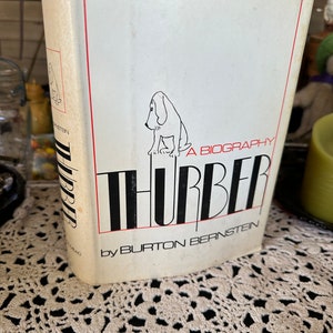 May include: A white book with a black and white illustration of a dog on the cover. The title of the book is "A Biography Thurber" by Burton Bernstein.