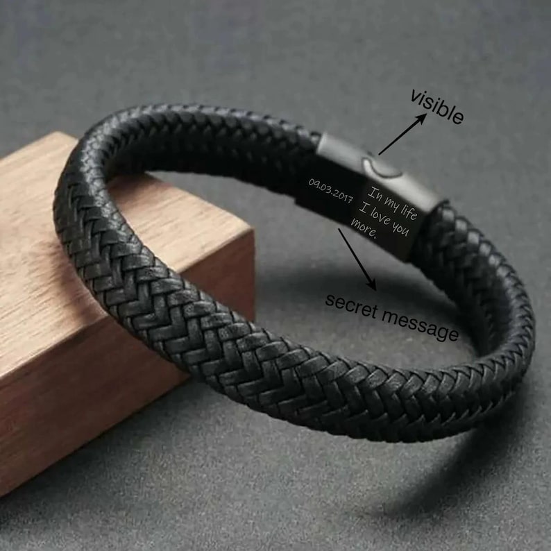 May include: A black braided leather bracelet with a metal clasp. The clasp is engraved with the date 09.03.2017 and the words "In my life I love you more."