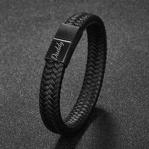 May include: Black braided leather bracelet with a magnetic clasp. The clasp is engraved with the word "Daddy" in a cursive font. The bracelet has a woven texture and a dark, matte finish.