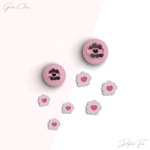 Puede incluir: Dos cortadores de galletas de plástico rosa en forma de flores con un corazón en el centro. Hay seis cortadores de galletas de flores rosas más pequeños con corazones en el centro dispersos alrededor de los cortadores más grandes. El texto "Gouda Cutters" está en la esquina superior izquierda de la imagen. El texto "Digital File" está en la esquina inferior derecha de la imagen.