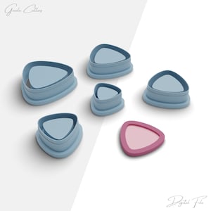 May include: Set of five blue triangle-shaped cookie cutters with a pink triangle-shaped cookie cutter in the center.  The cookie cutters are for making triangle-shaped cookies.
