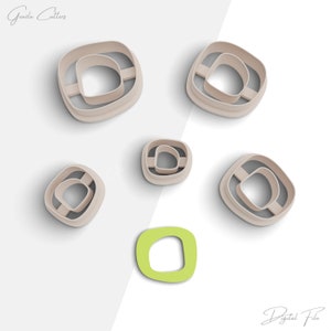 May include: Set of six cookie cutters in various sizes, featuring a rounded square shape with a smaller rounded square cutout inside. The cutters are beige and are arranged on a white background. The image also includes a green cookie cutter in the same shape.