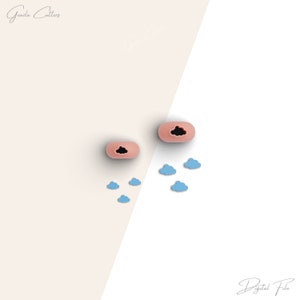 Könnte beinhalten: Zwei rosa Silikon-Ausstecher in Wolkenform mit schwarzen Wolkenausschnitten. Es gibt sechs kleinere blaue Silikon-Ausstecher in Wolkenform, die um die größeren Ausstecher herum verstreut sind.