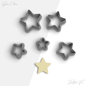 May include: Set of six gray star-shaped cookie cutters, with a yellow star-shaped cookie cutter in the center.  The cookie cutters are arranged in a circle around the cookie.