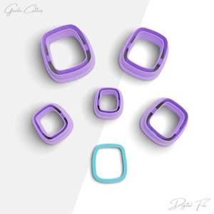 May include: Set of six purple and one blue plastic cookie cutters shaped like rounded squares. The cutters are arranged on a white background.