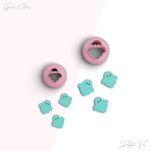 Op de afbeelding: Twee roze spookvormige koekjessnijders en zes turquoise spookvormige uitsparingen worden weergegeven op een lichtroze achtergrond. De koekjessnijders hebben een cirkelvormig ontwerp met een spookvormige uitsparing in het midden. De tekst "Gezila Cutters" en "Digital File" staan in de afbeelding.