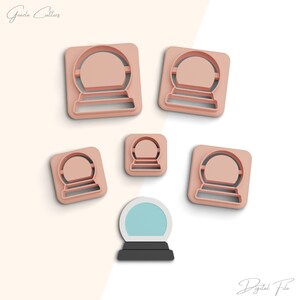 Op de afbeelding: Vijf roze plastic koekjesvormen in de vorm van sneeuwbollen, met een zesde sneeuwbol koekjesvorm in het midden, maar deze is blauw en zwart.