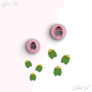 May include: Two pink cookie cutters shaped like a pot of gold with a lid. Five green cookie cutters shaped like a pot of gold with a lid.